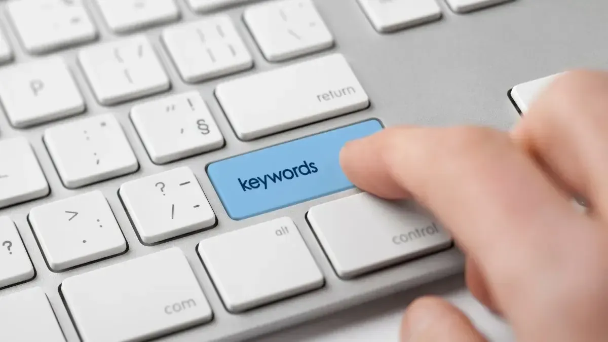 A person is pressing a blue key on a keyboard that says keywords.