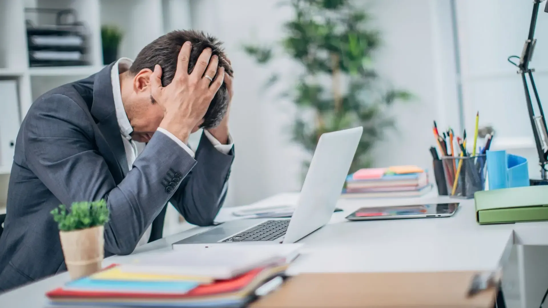 Stressed businessman holding head at office desk with laptop.