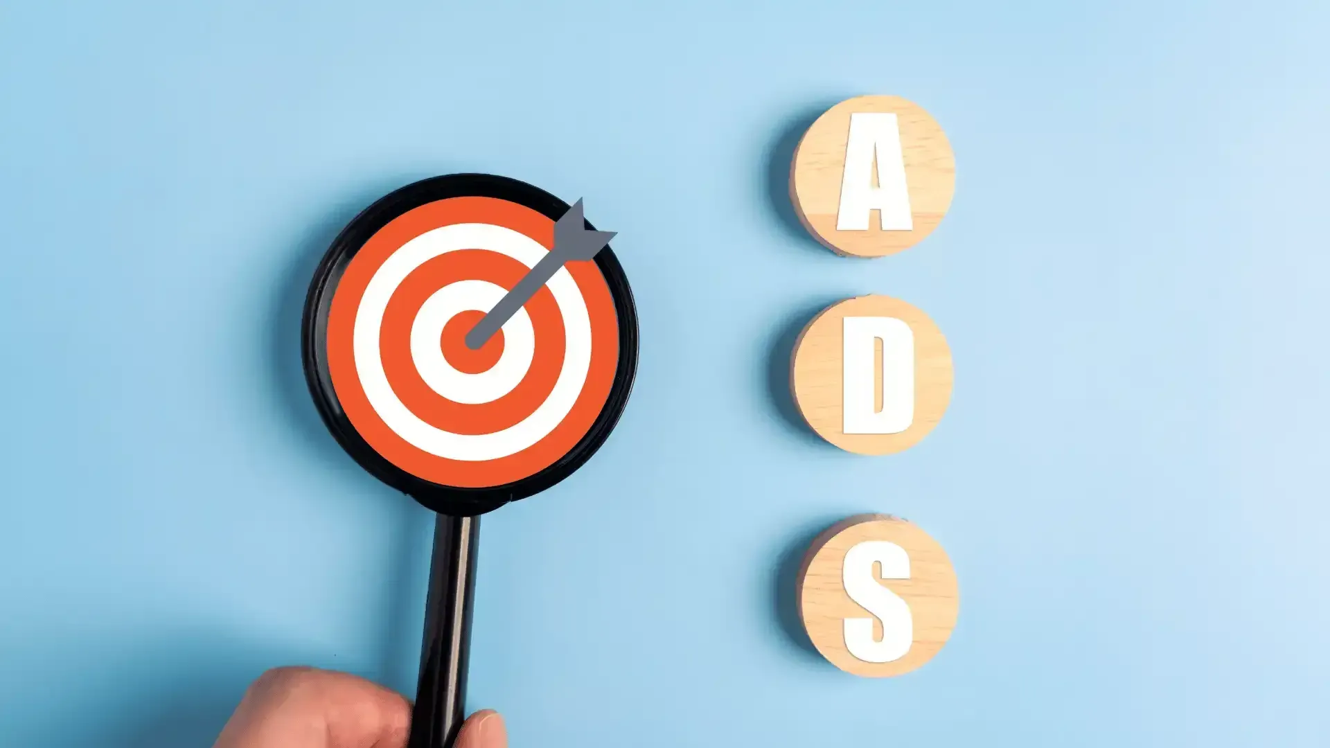 A person is holding a magnifying glass in front of a target with a dart in it.