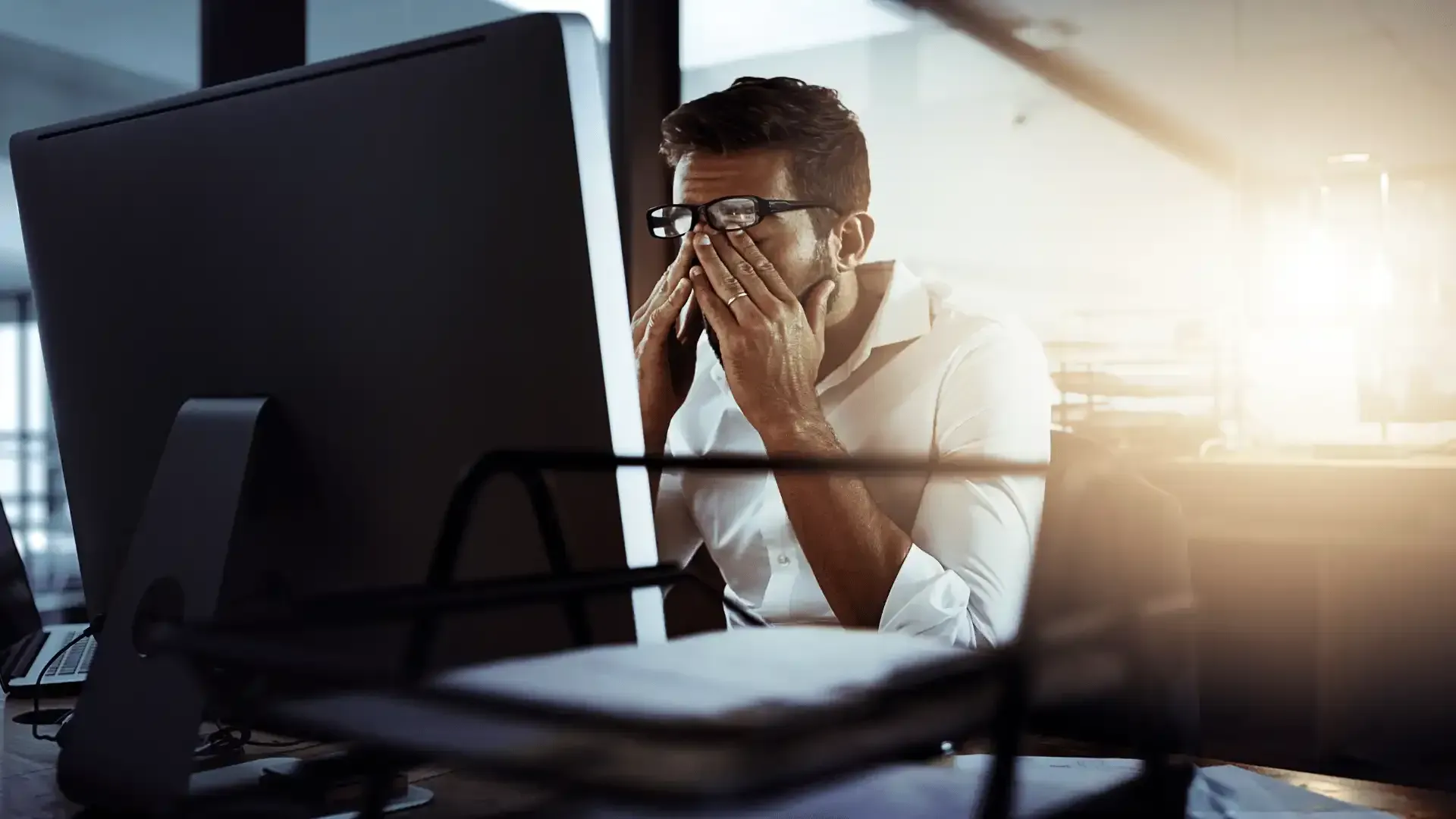 a man covering his face while looking at a computer screen