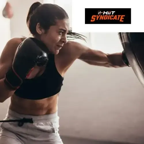 Woman boxing, punching pad in a gym. Athletic, focused expression. HIIT Syndicate logo.