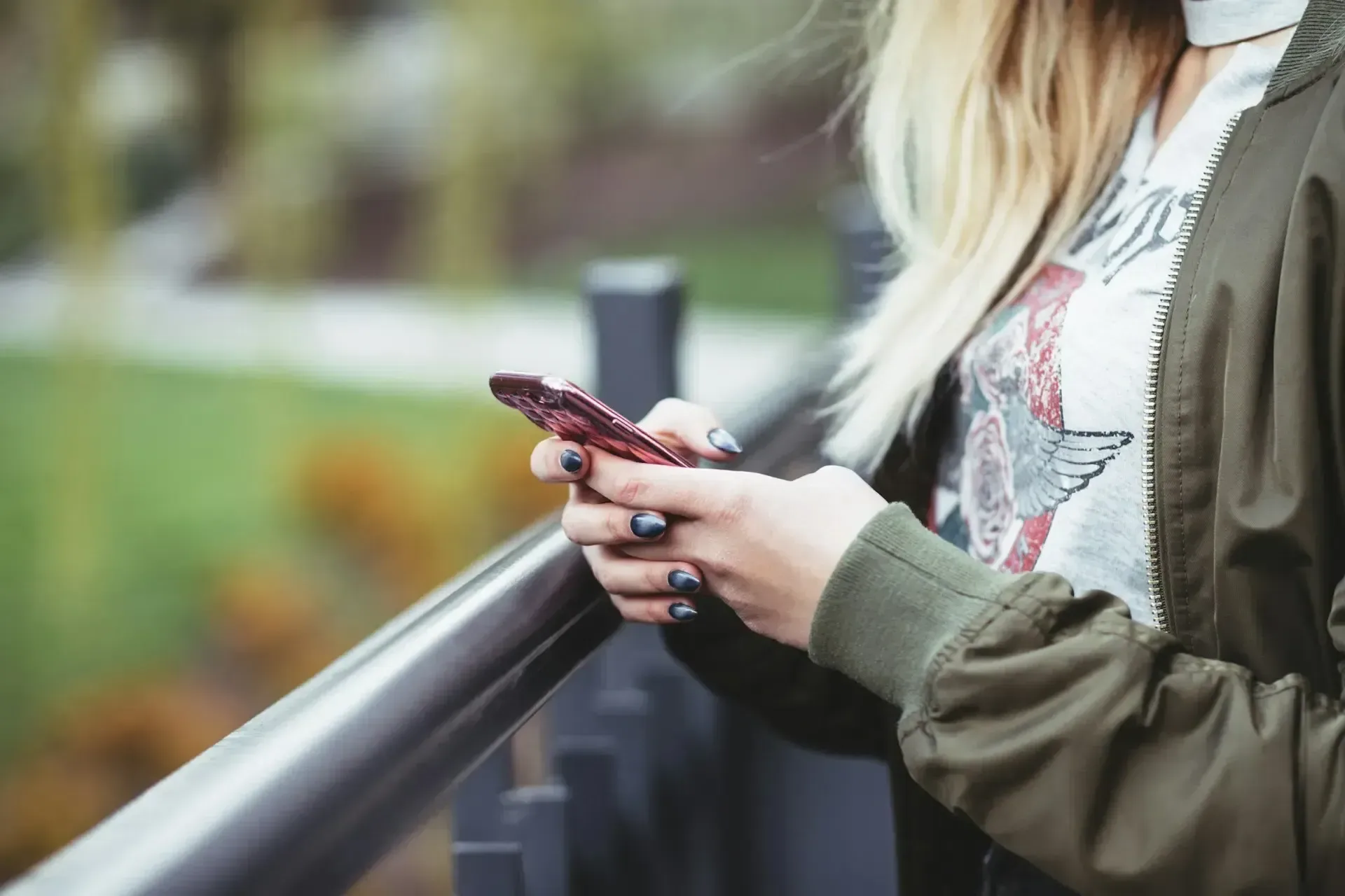 A woman is standing on a bridge looking at her cell phone.