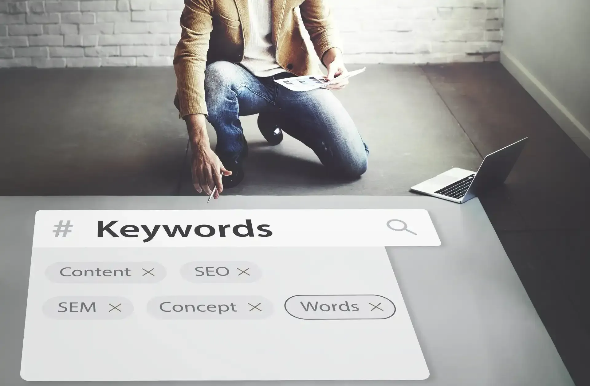 a man is kneeling on the floor searching for keywords on a laptop .