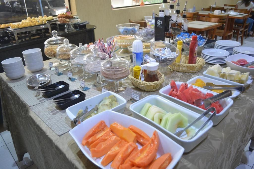 Buffet de café da manhã com pratos de frutas, doces, sucos e pratos cobertos em uma mesa de jantar.