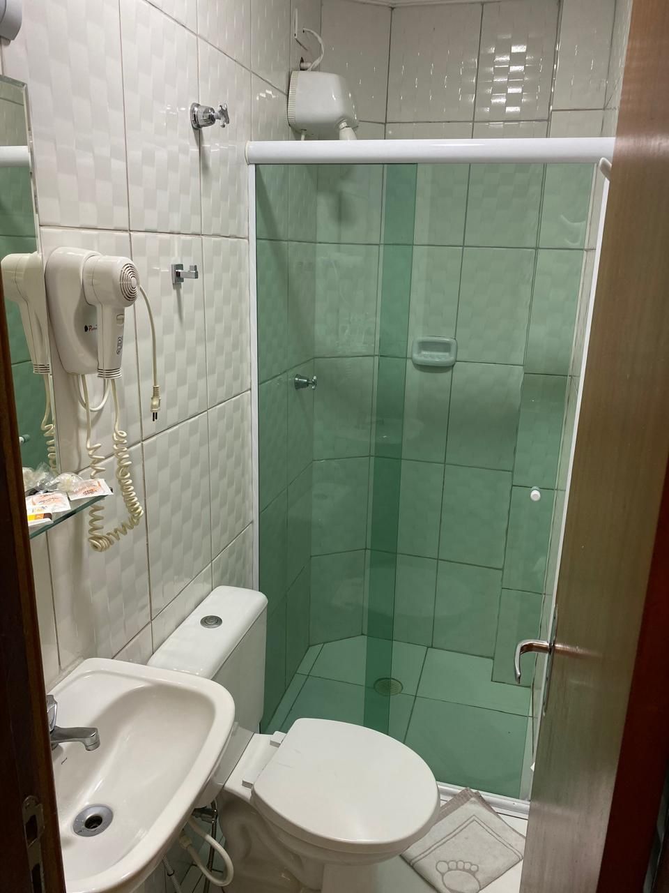 Banheiro pequeno com vaso sanitário, pia e box de vidro verde.