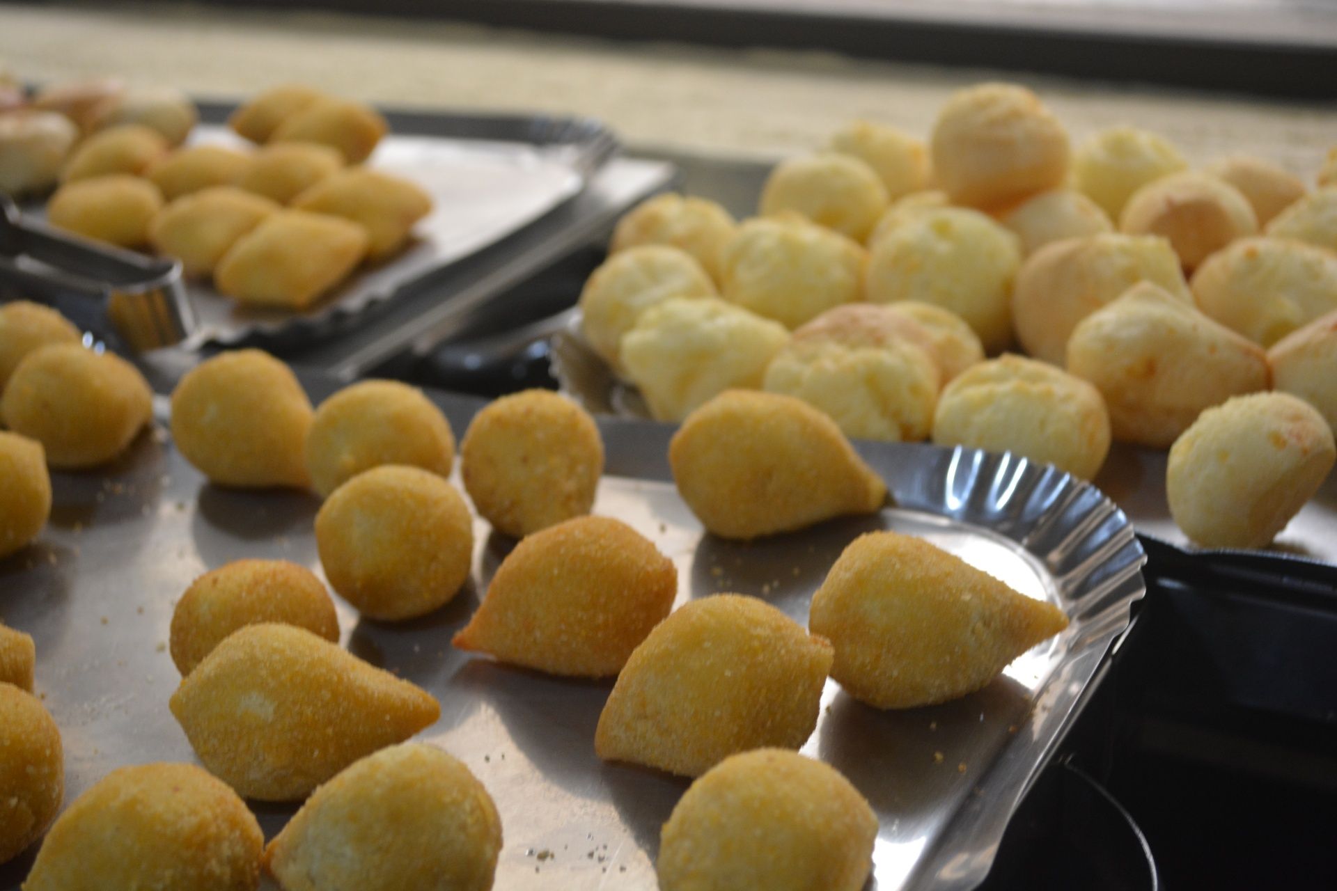 Bandejas de bolinhos de massa frita dourados e pastéis sobre uma mesa de metal