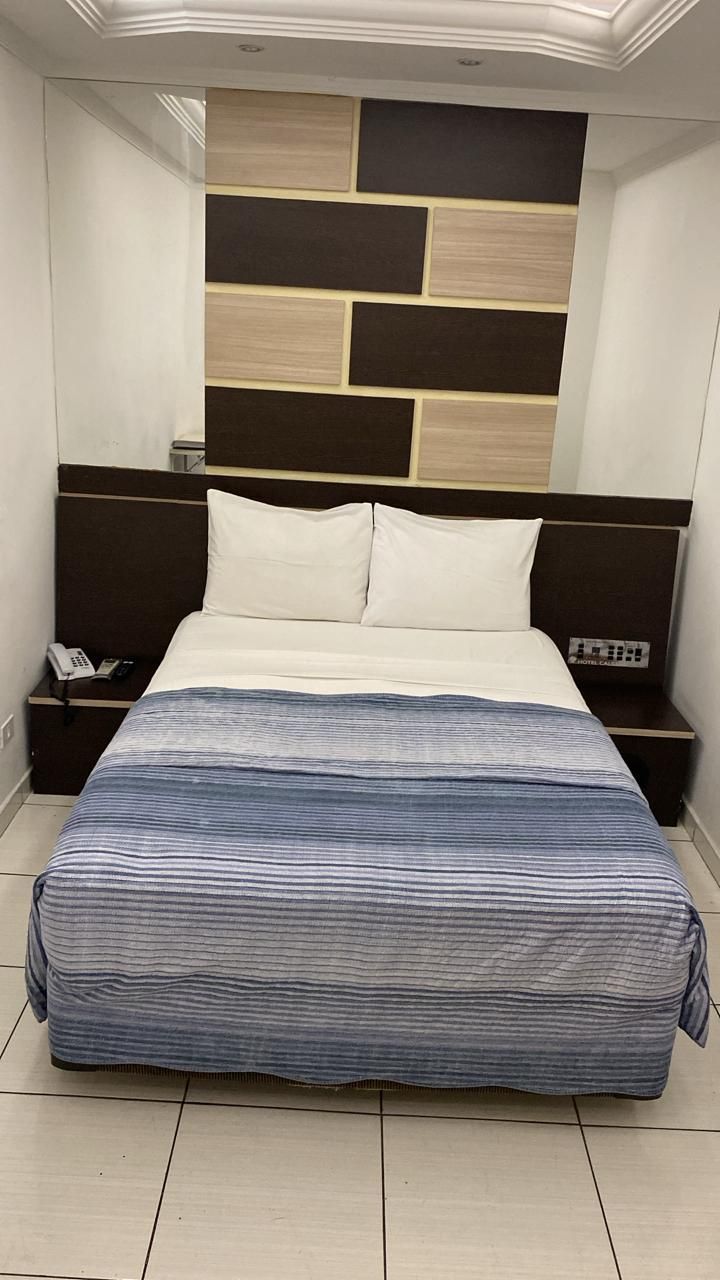 Quarto pequeno com cama, cobertor listrado azul, travesseiros brancos e painéis de parede em tons de marrom e creme.