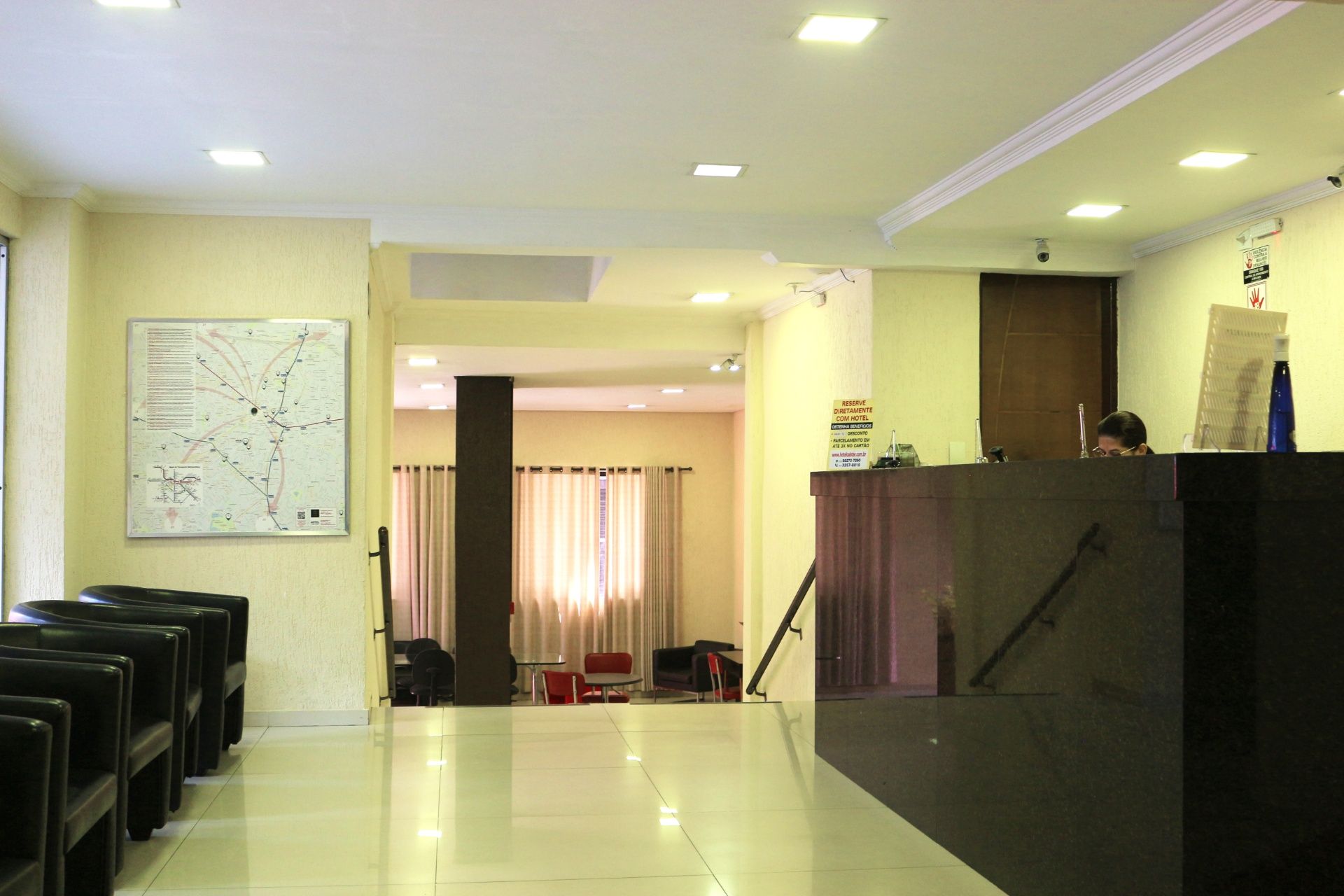 Hall de entrada luminoso com sofás, balcão de recepção e um corredor com cortinas ao fundo.