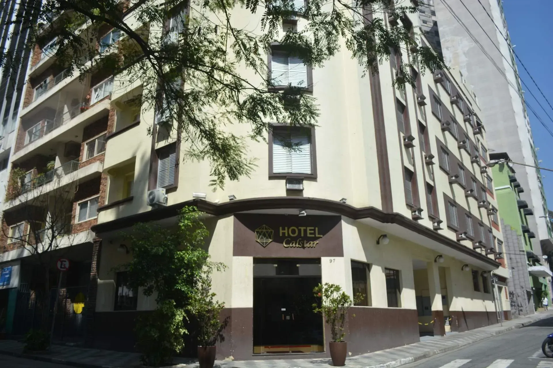 Vista da esquina de um prédio de hotel bege com varandas e uma placa escura em um toldo.