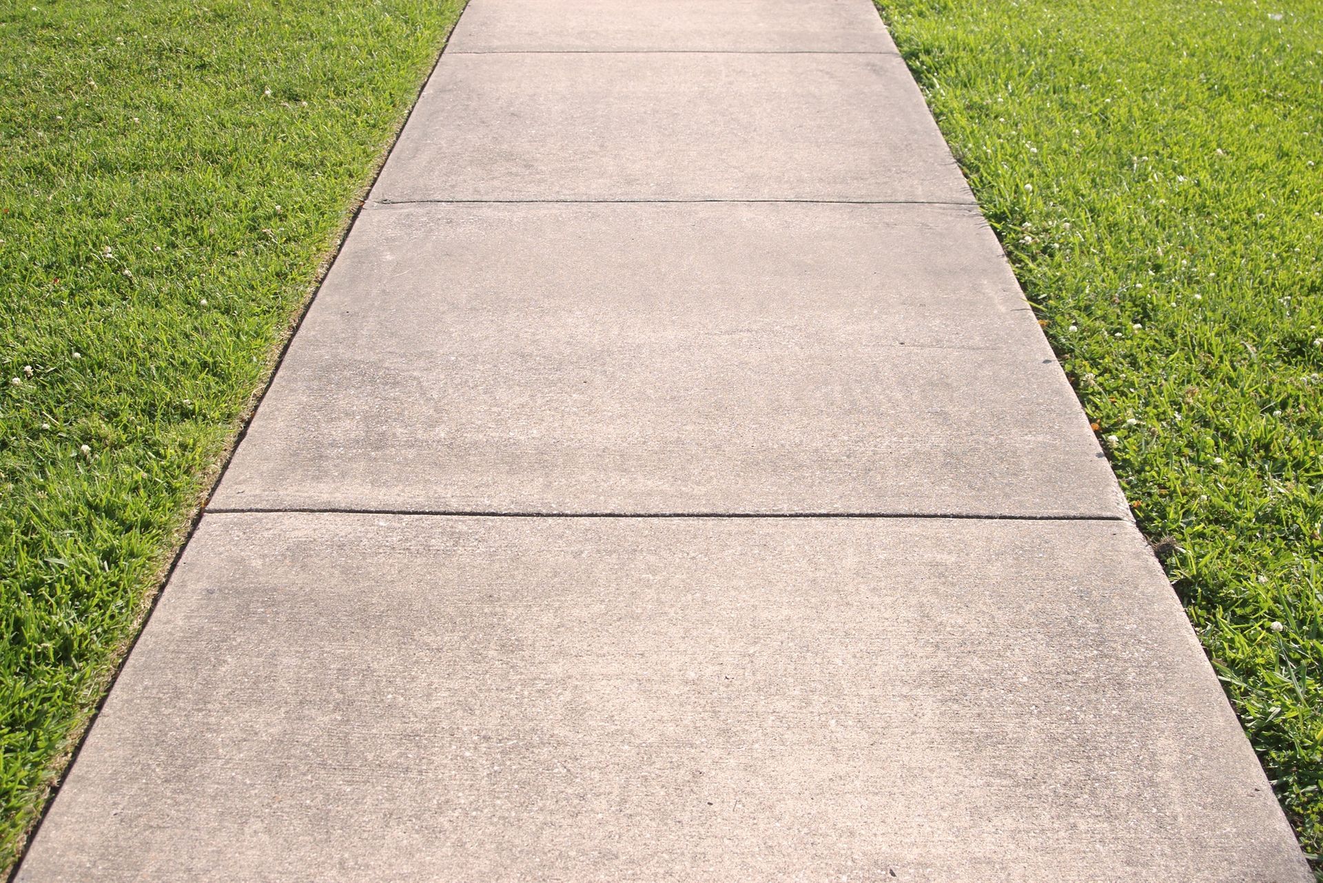 A concrete driveway leads to a two-car garage of a house surrounded by a green lawn and neatly trimmed landscaping.