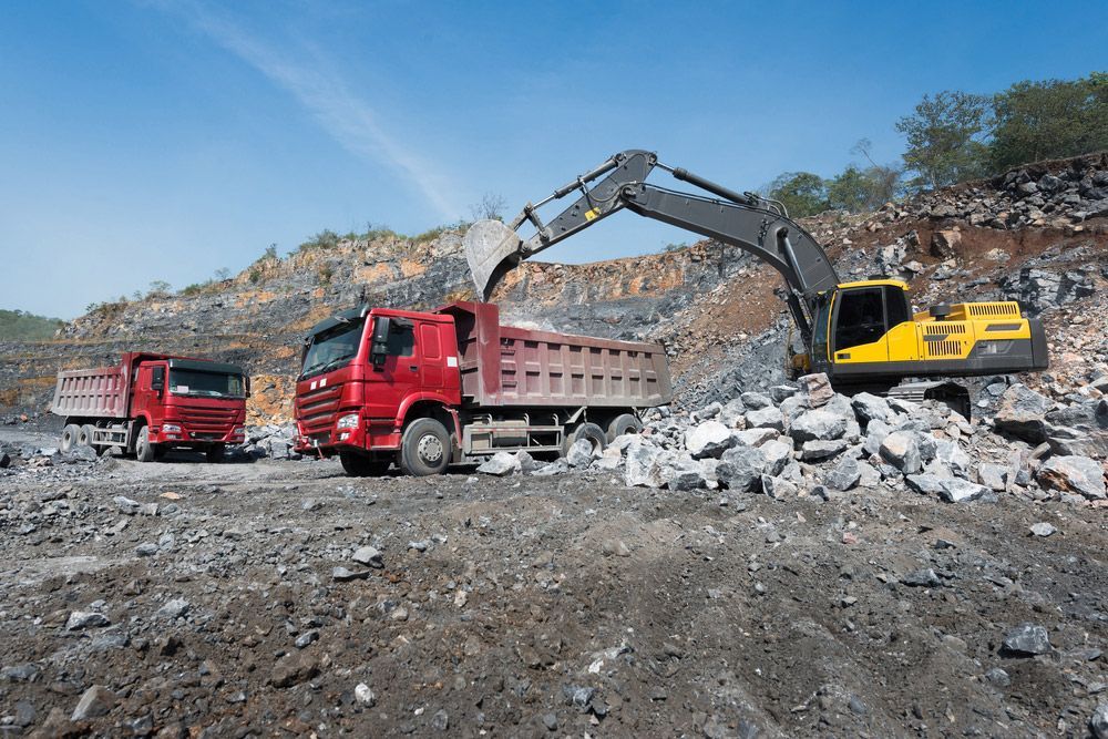 A dump truck is being loaded with rocks by an excavator in a quarry