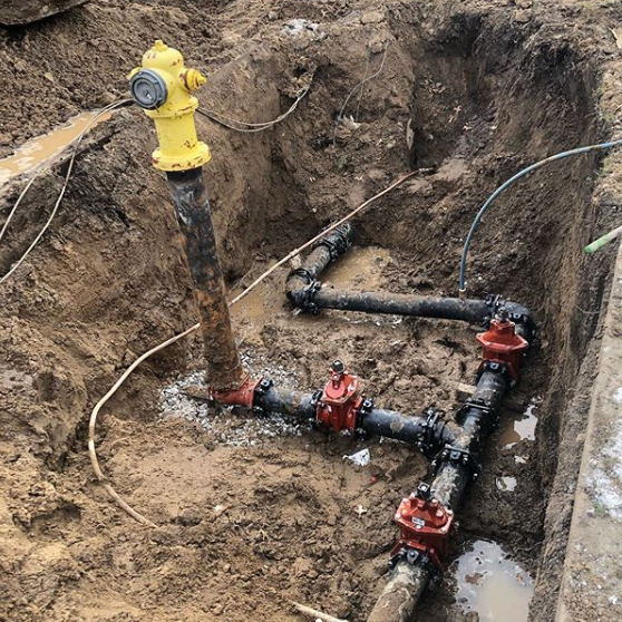 A yellow pipe is sitting in the dirt next to a bunch of pipes