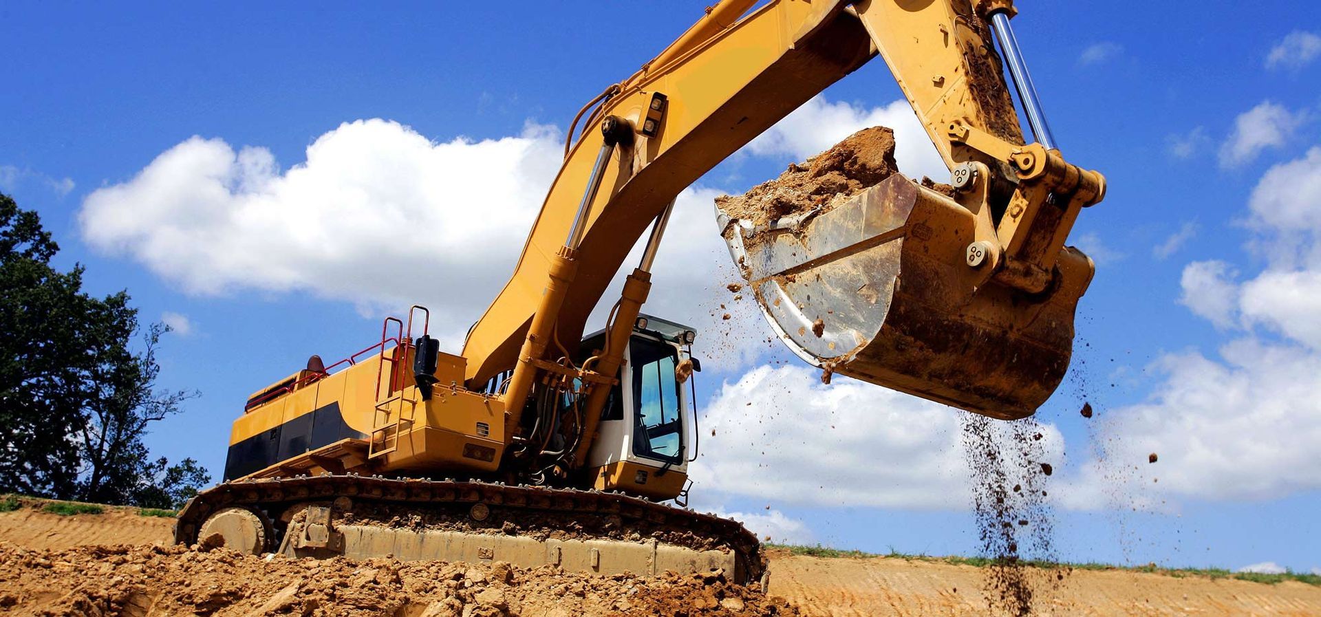 A yellow excavator is digging a hole in a dirt field