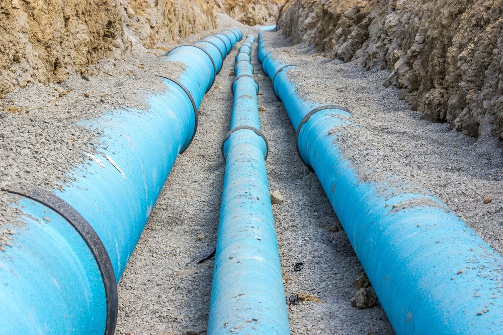 A row of blue pipes are lined up in a trench