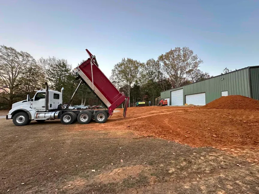 A dump truck is loading dirt into a pile in a parking lot.