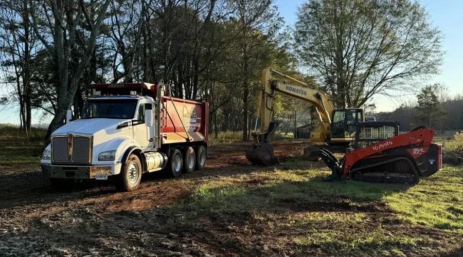 A dump truck and an excavator are parked in a dirt field.