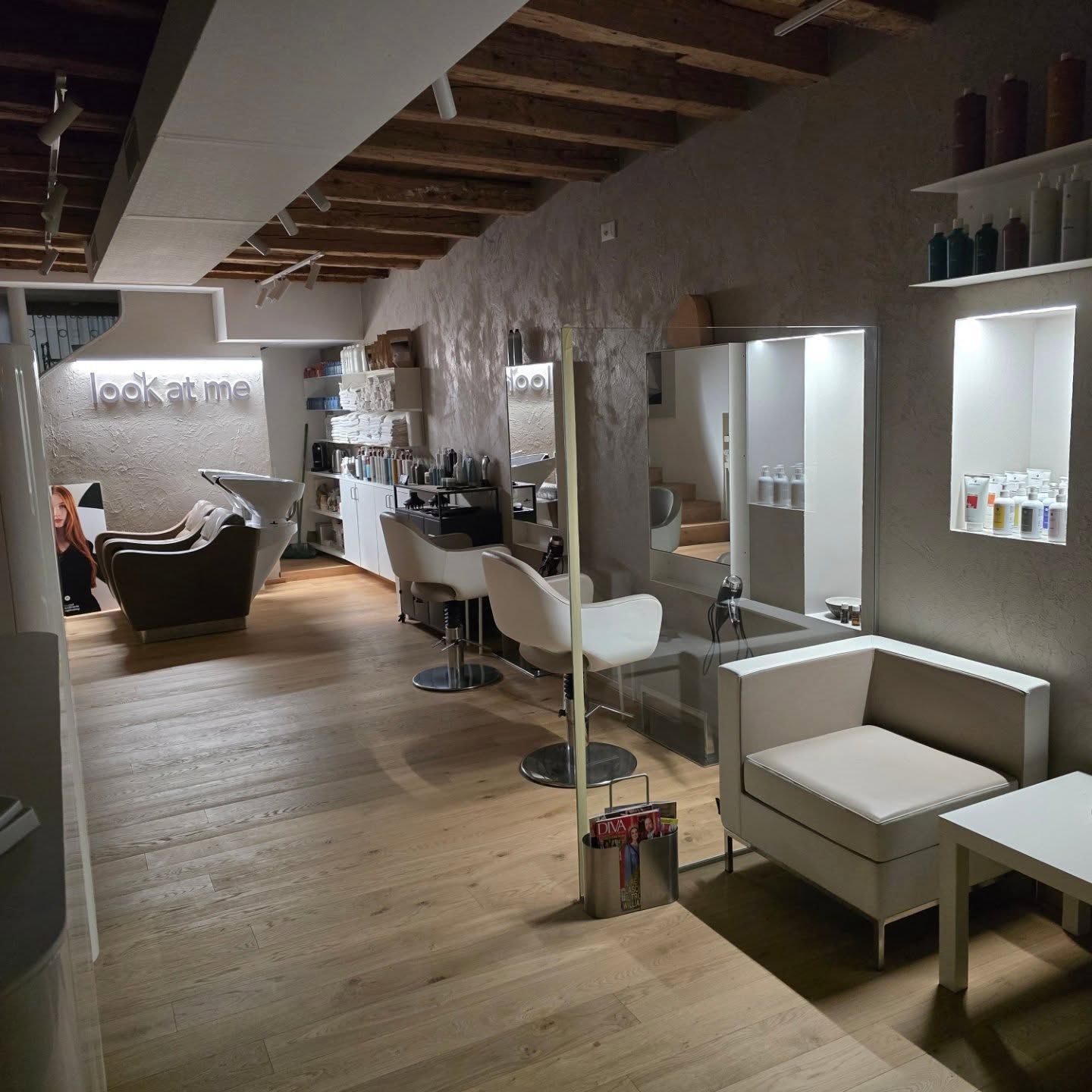 Interni moderni di un salone con poltrone da parrucchiere, specchi, lavabi e pavimenti in legno dalle tonalità calde.