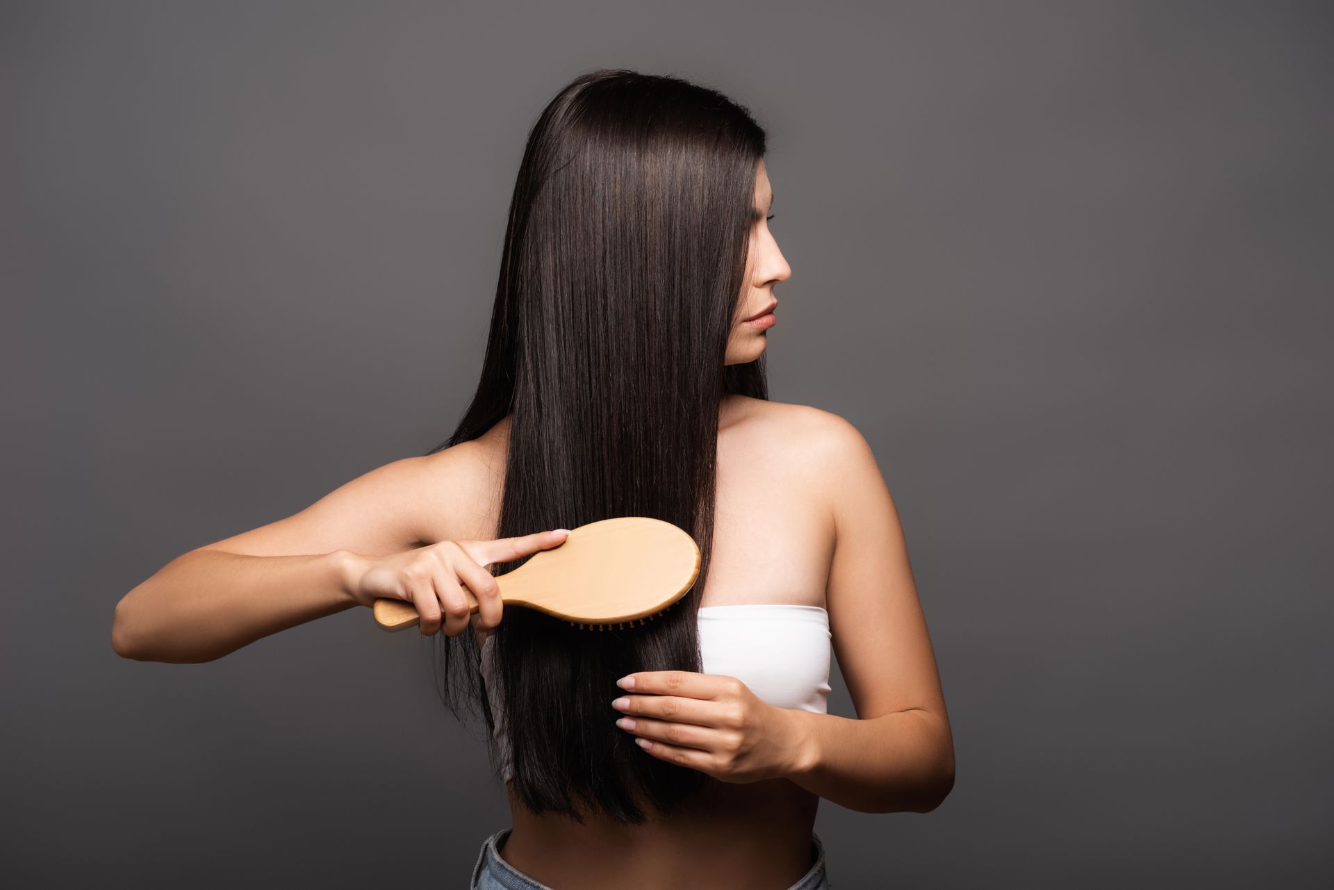 Donna con lunghi capelli scuri che li spazzola con una spazzola di legno su uno sfondo grigio