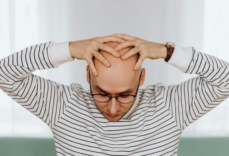 Uomo che tiene la testa tra le mani per frustrazione: il legame tra calvizie e depressione