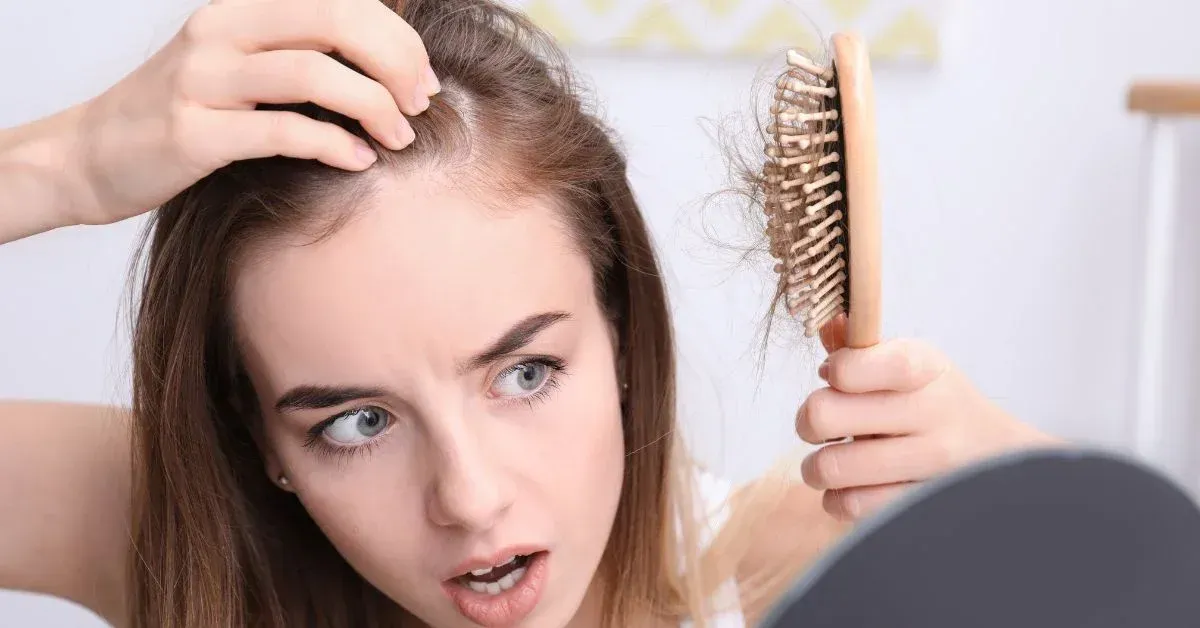 Ragazza che guarda allarmata i capelli rimasti sulla spazzola: caduta dei capelli, quando preoccuparsi
