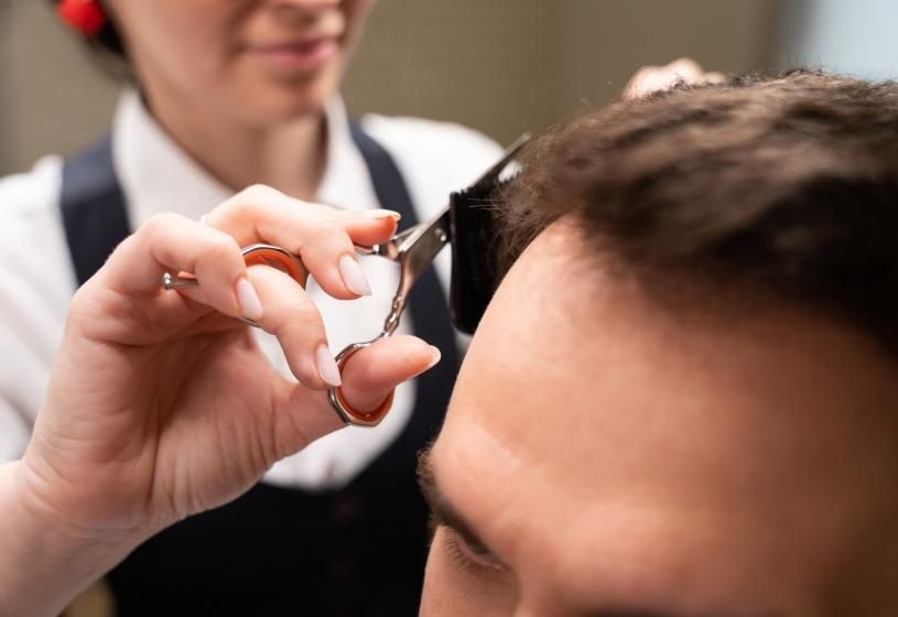 Professionista che taglia i capelli per pareggiarli dopo l'applicazione della patch cutanea: vantaggi e controindicazioni