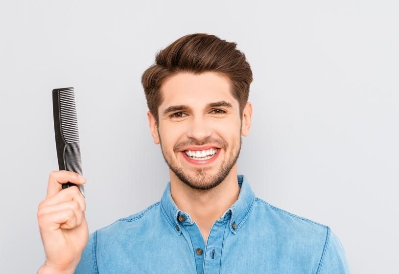 Uomo sorridente con pettine in mano: 3 rimedi naturali efficaci per la perdita dei capelli maschile