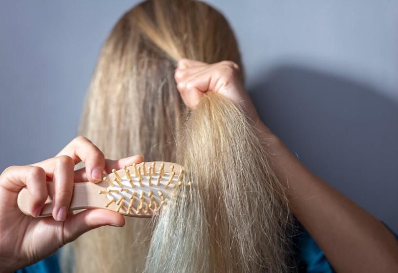 Donna vista di spalle che spazzola con cura i capelli lunghi biondi: 7 consigli pratici per curare i capelli fini e sottili