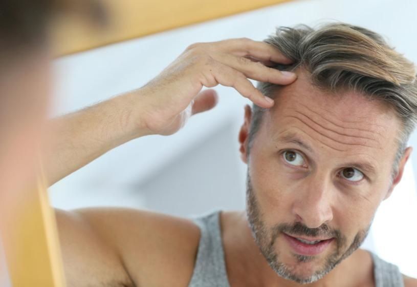 Uomo di profilo che controlla i capelli davanti allo specchio: la patch cutanea come soluzione