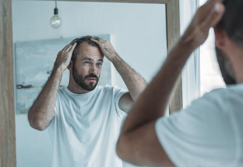 Uomo che si controlla i capelli al bagno allo specchio: guida ai migliori prodotti per infoltire i capelli