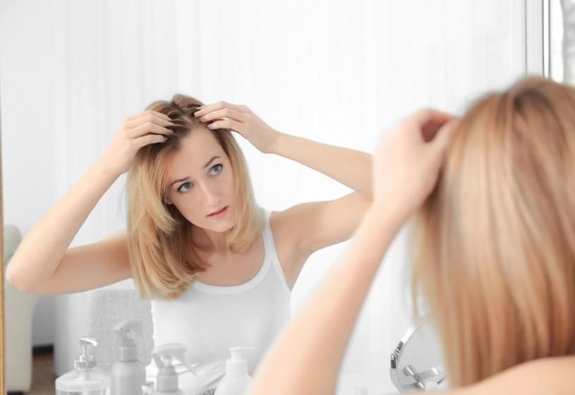 Donna bionda che esamina preoccupata il diradamento alla radice allo specchio: cosa mangiare per nutrire, infoltire i capelli