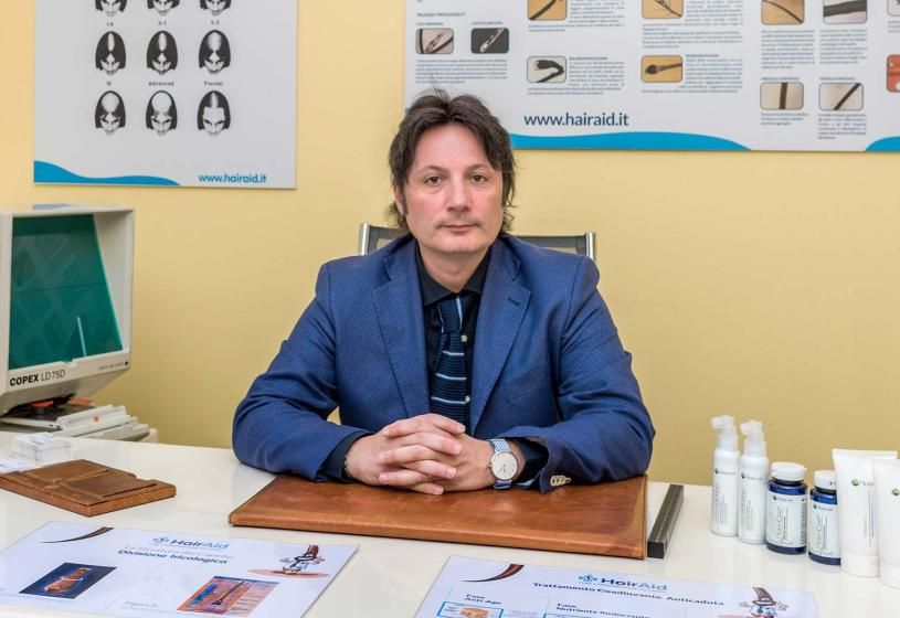 Direttore e fondatore di HairAid Marco Latini in studio con poster informativi sulla perdita dei capelli