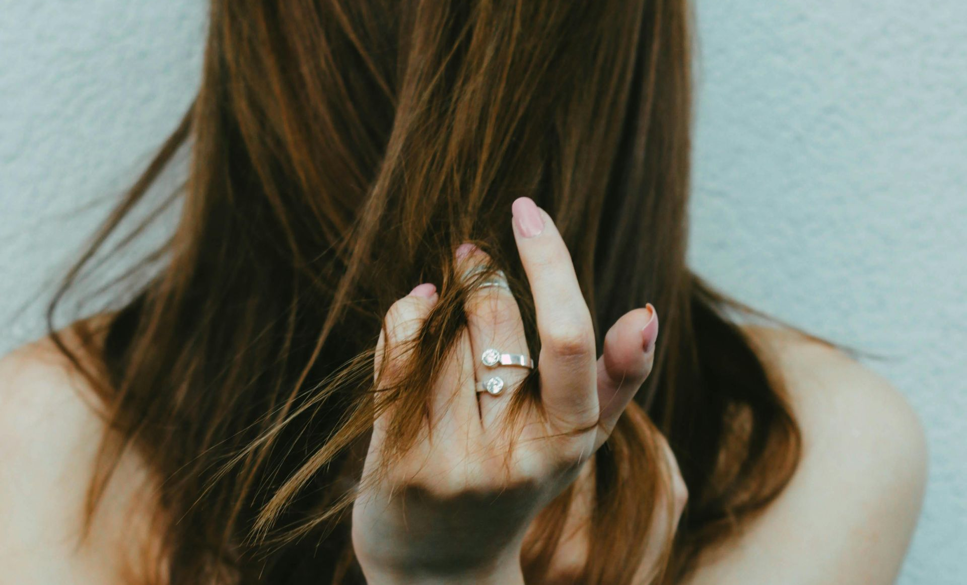 Donna vista di spalle che passa le dita tra i capelli lunghi castani: 5 rimedi efficaci per eliminare i capelli grassi