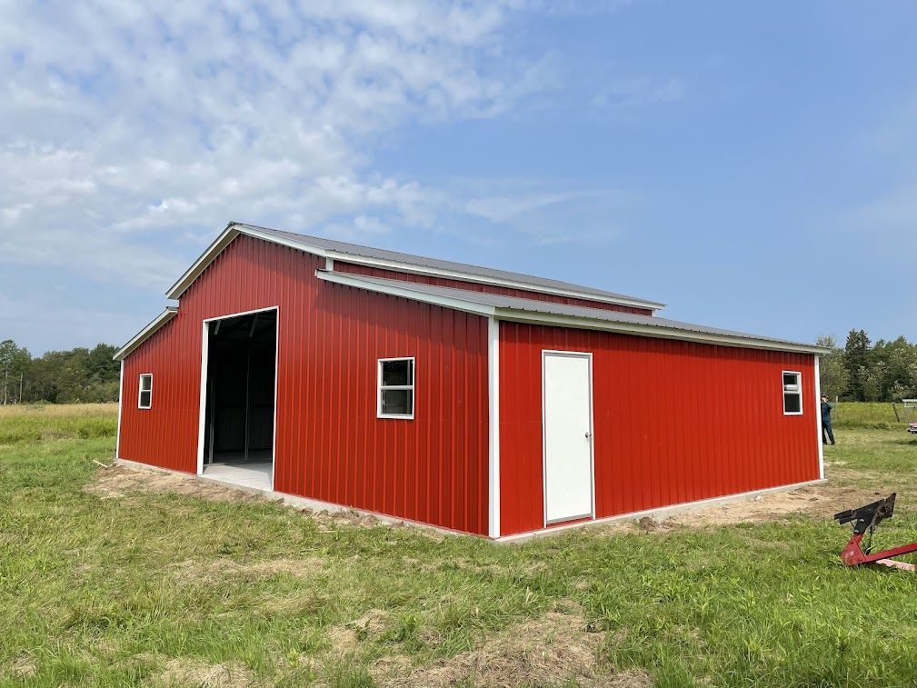 a large red barn is sitting in the middle of a grassy field .