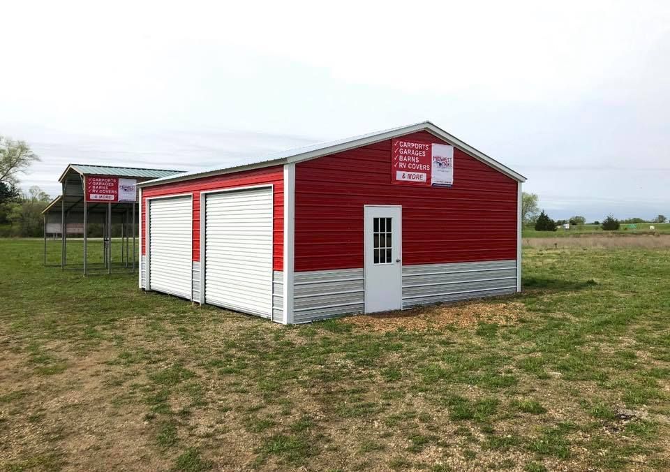 a red and white garage is sitting in the middle of a grassy field .