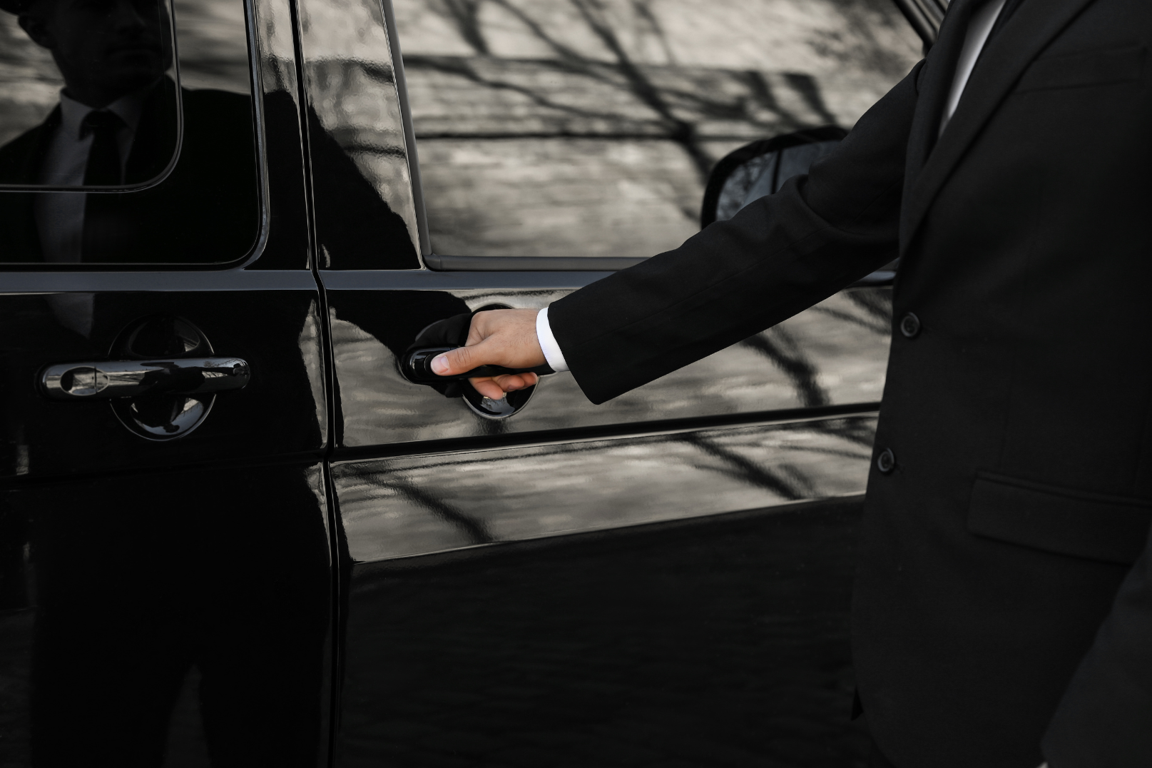 A man in a suit is opening the door of a black car.