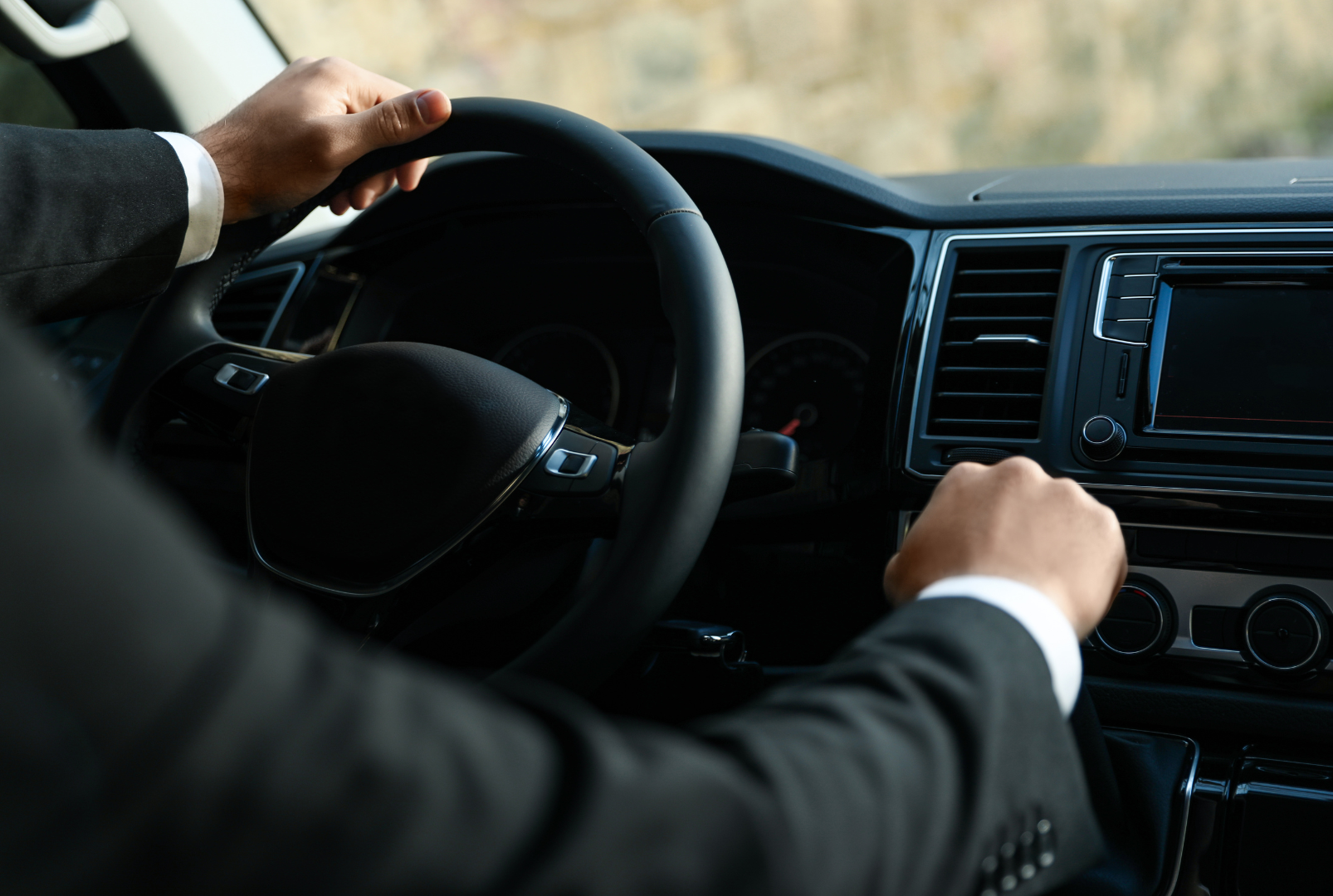 A man in a suit and tie is standing in front of a black car.