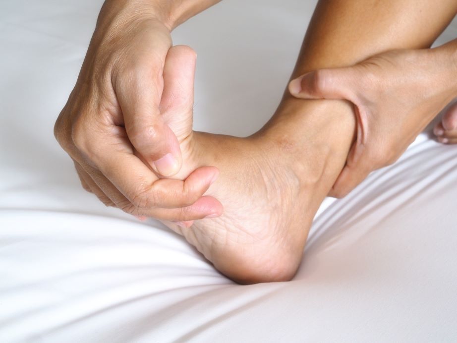Person holding their ankle, possibly in pain, on a white bed in Hope Mills, NC.