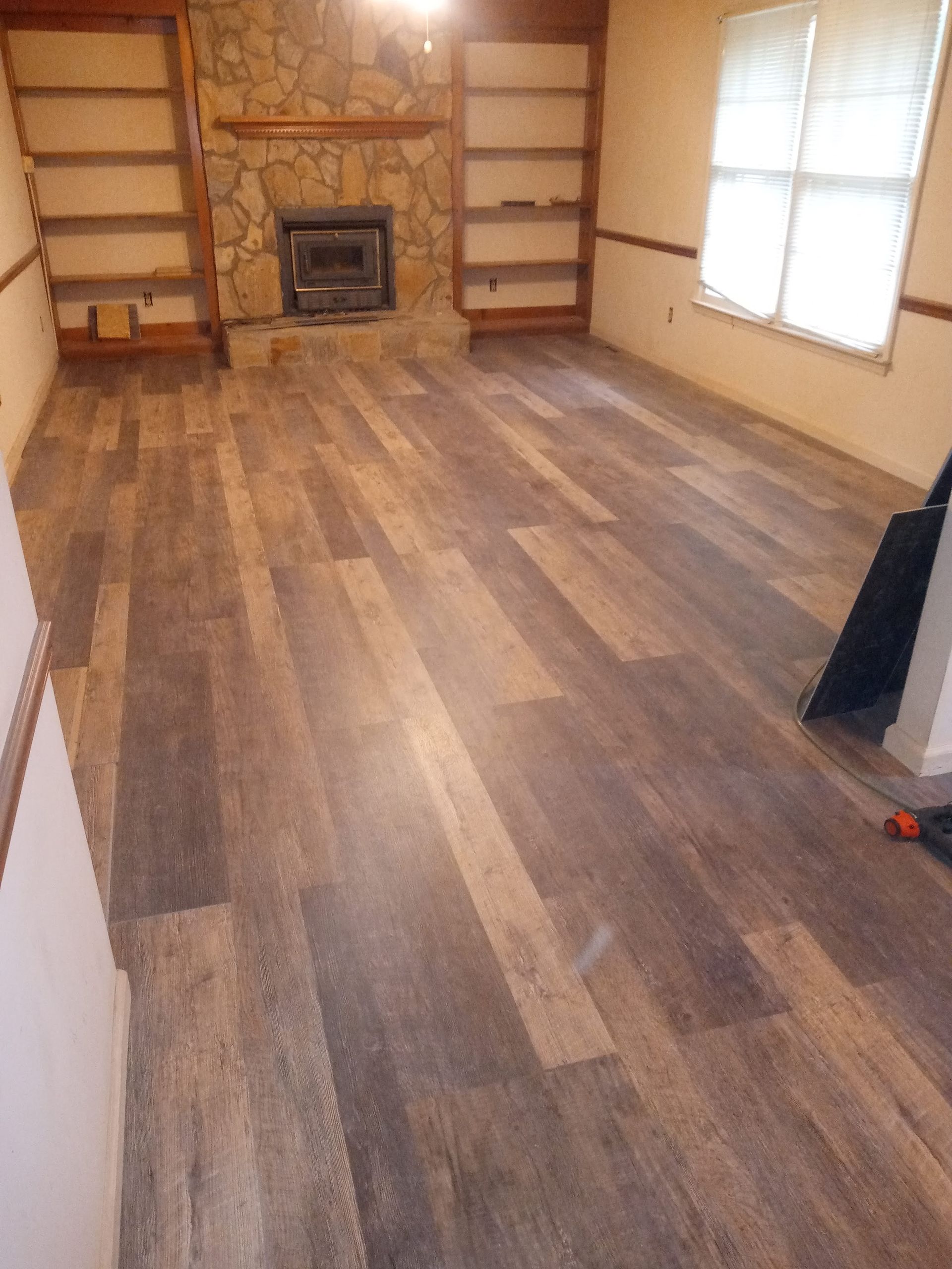 Hand installing wood flooring plank with a white spacer strip beside it