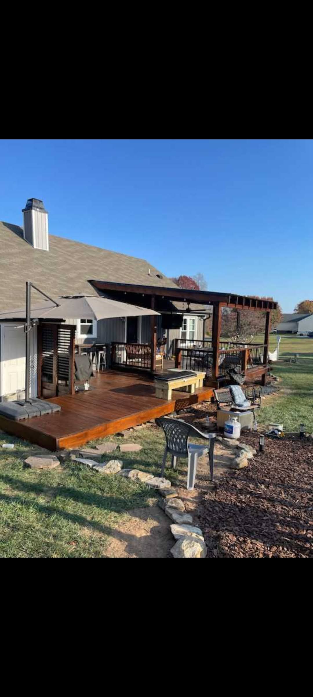 Freshly painted wooden deck under construction beside a gray house, with white railing and blue sky.