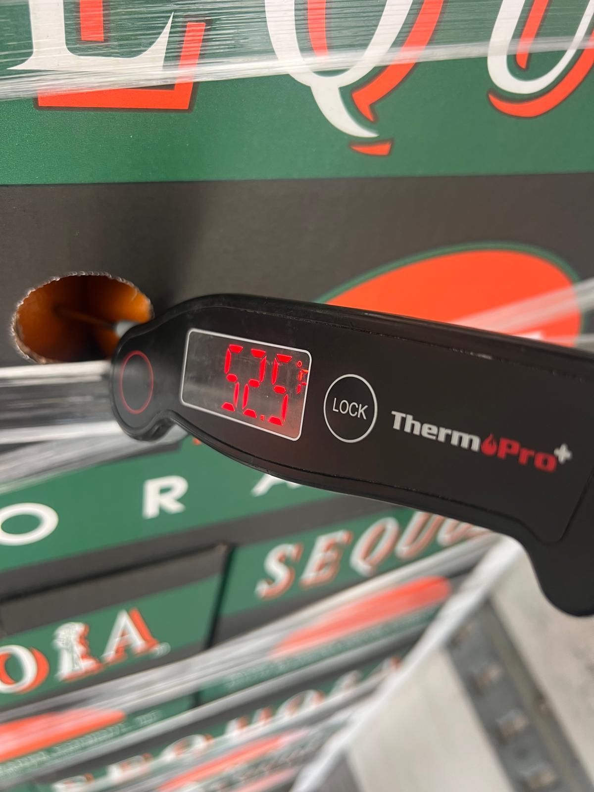 Digital thermometer reading 39°C held near stacked boxes in a store aisle