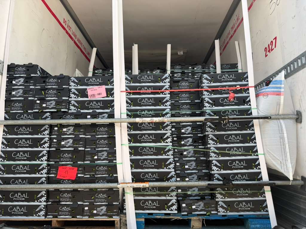 Stacks of black crates loaded in a truck trailer, with white support poles and red straps inside.
