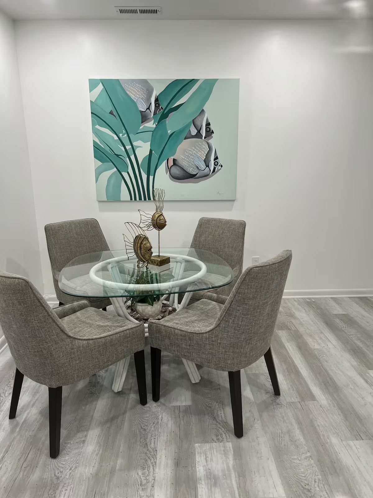 A dining room with a glass table and chairs and a painting on the wall.