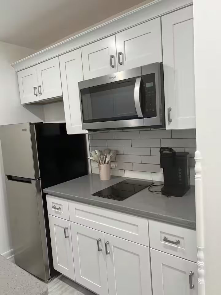 A kitchen with white cabinets , stainless steel appliances , a refrigerator , microwave and stove.