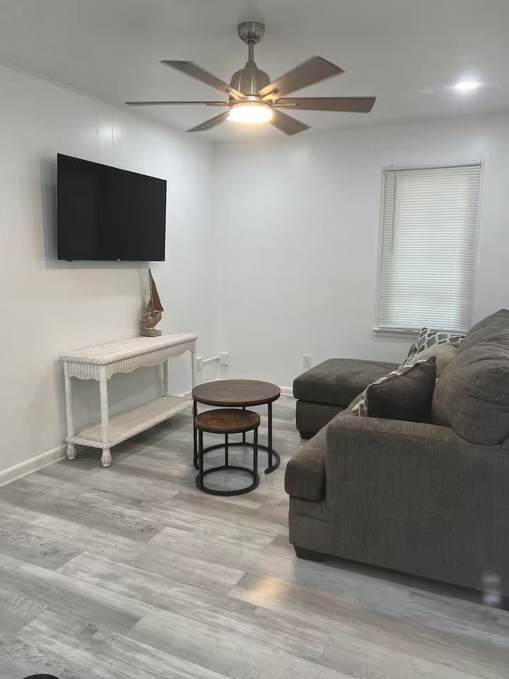 A living room with a couch , table , television and ceiling fan.