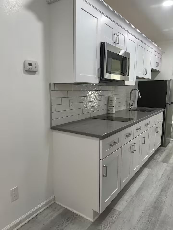 A kitchen with white cabinets , a sink , a microwave , and a refrigerator.