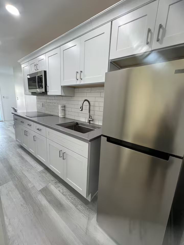 A kitchen with white cabinets , a stainless steel refrigerator , a sink , and a microwave.