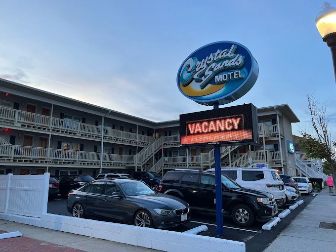 A motel with cars parked in front of it and a vacancy sign.