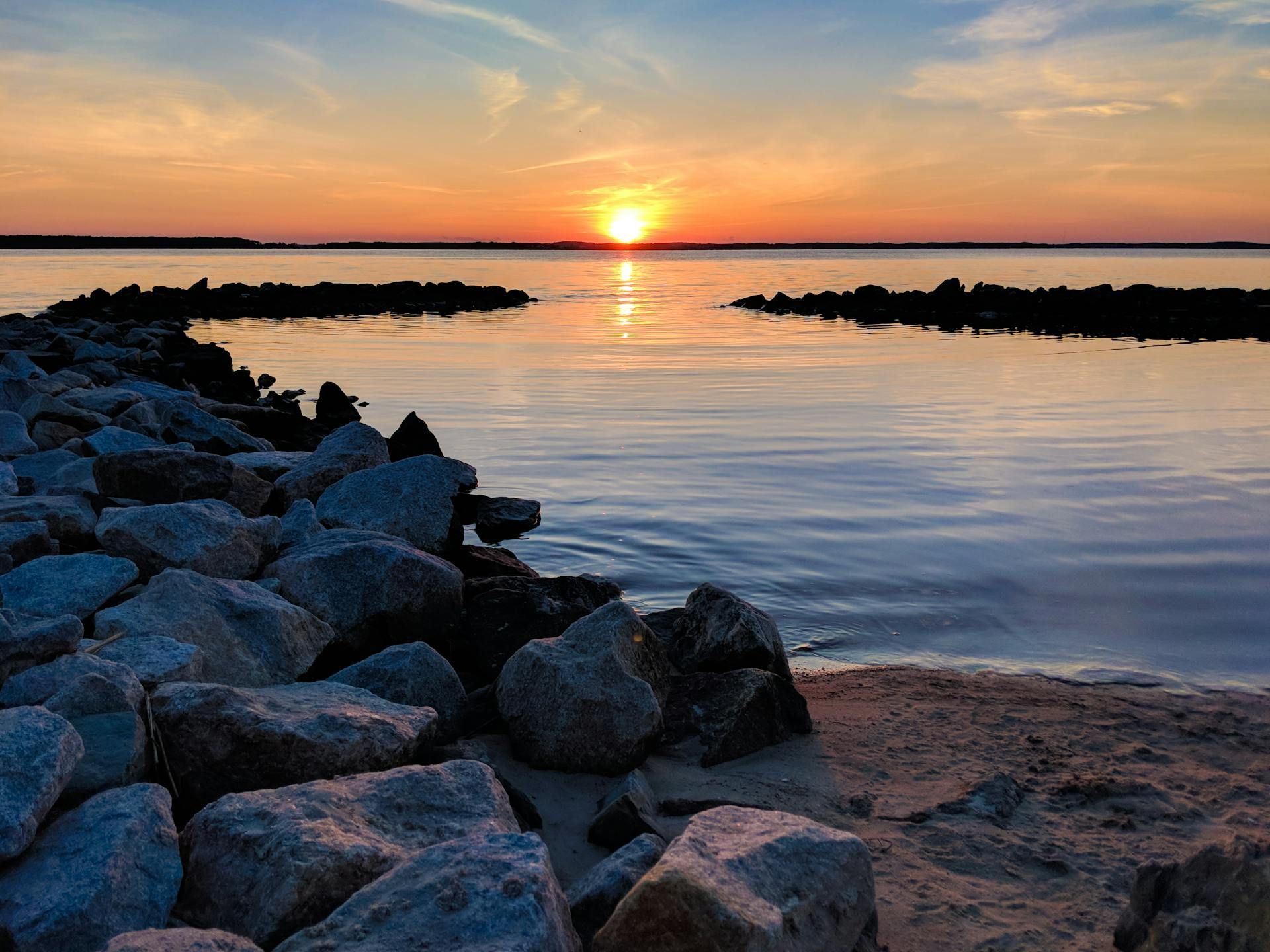 A sunset over a body of water with rocks in the foreground.