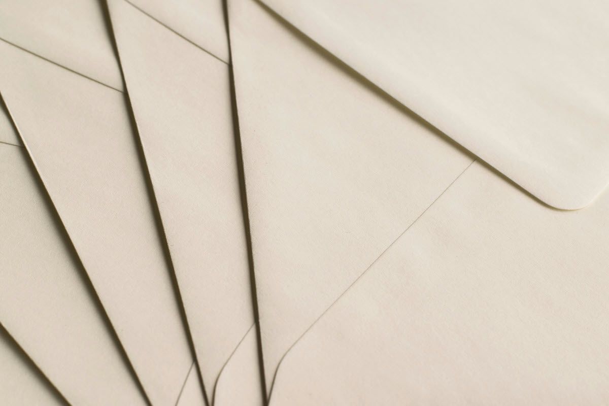 Cream-colored envelopes stacked, fanned slightly, with shadows and subtle folds visible.