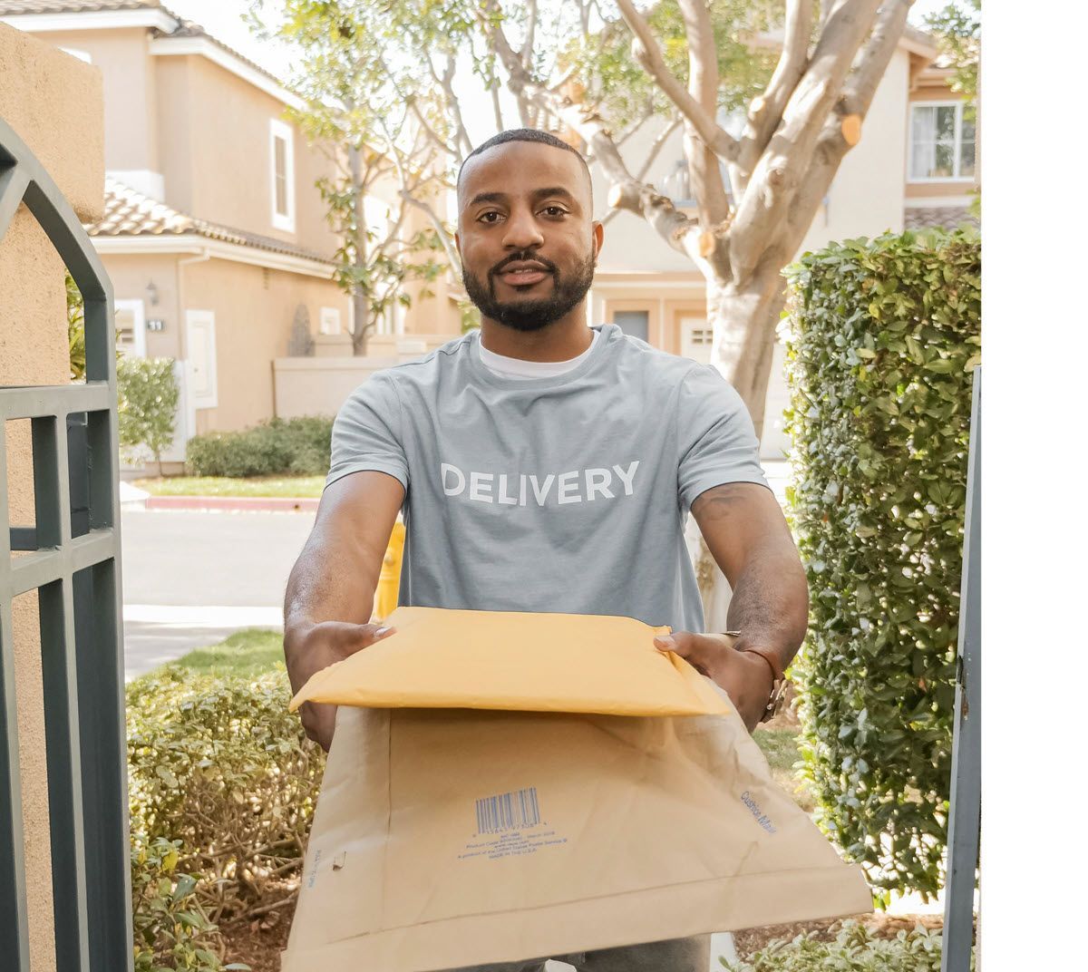 Delivery man holding package, standing at a gate. Wearing gray shirt, brown package, outside.